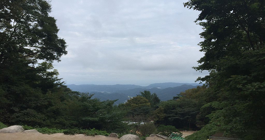 A peaceful mountain landscape seen from the entrance of Seokguram Grotto, framed by lush trees and an overcast sky.