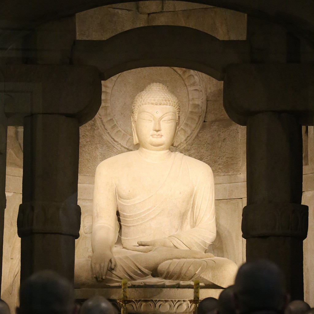 A serene view of Seokguram Grotto in South Korea, showcasing the intricately carved stone Buddha seated inside the ancient Buddhist temple, with soft natural lighting highlighting its features.